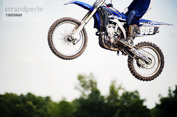 Niedriger Teil eines Motorradfahrers führt Stunt in der Luft gegen klaren Himmel aus
