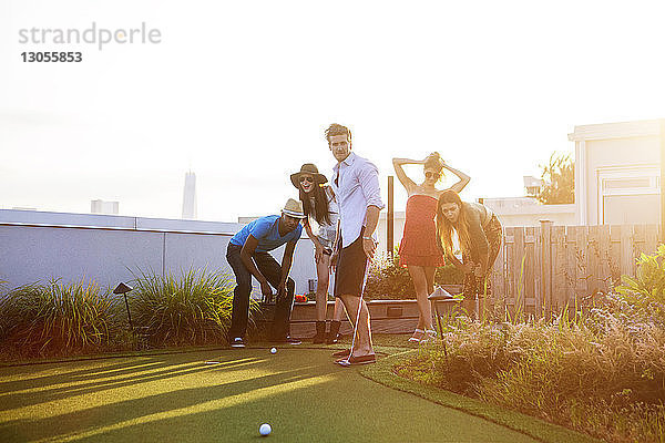Freunde schauen auf den Golfball  während sie bei Sonnenuntergang auf der Terrasse des Gebäudes stehen