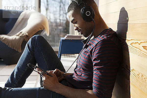 Mann benutzt Smartphone  während er zu Hause Musik über Kopfhörer hört