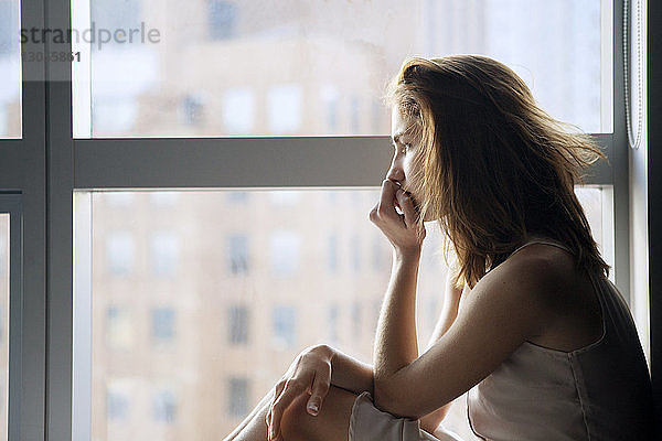 Seitenansicht einer nachdenklichen Frau am Fenster sitzend