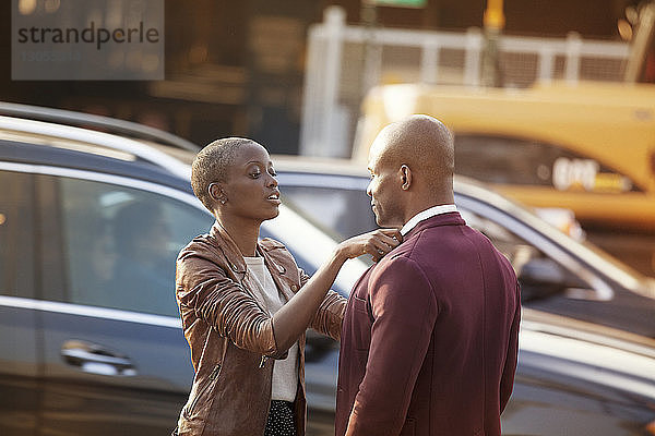 Frau stellt den Kragen eines Mannes ein  während sie auf der Straße gegen ein Auto steht