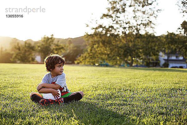Junge sitzt mit Fussball auf Grasfeld im Park