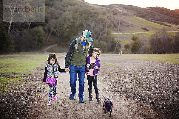 Vater und Töchter gehen mit Hund auf Wanderweg gegen Berg