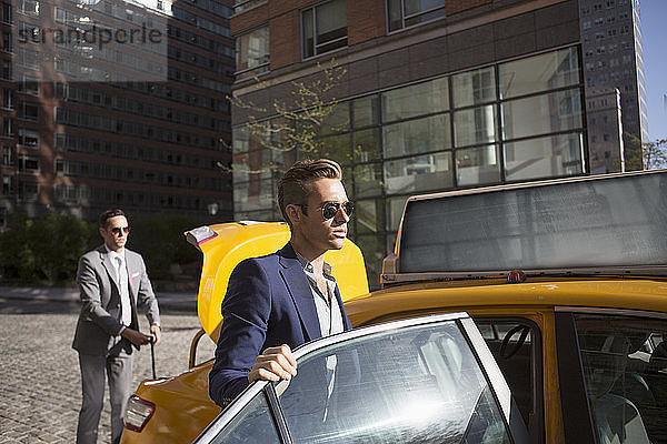 Geschäftsmann steigt mit einem Kollegen im Hintergrund in ein Taxi