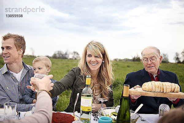 Glückliche Familie und Freunde essen beim Picknick gegen den Himmel