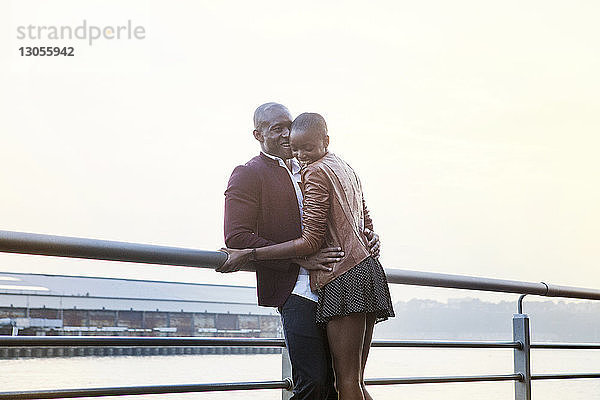 Fröhliches Paar steht am Geländer am Pier vor klarem Himmel