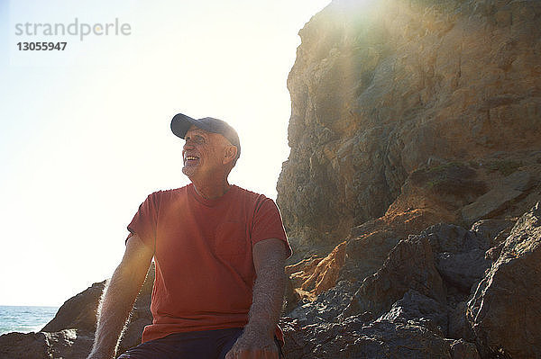 Glücklicher älterer Mann sitzt an einem sonnigen Tag auf einem Felsen
