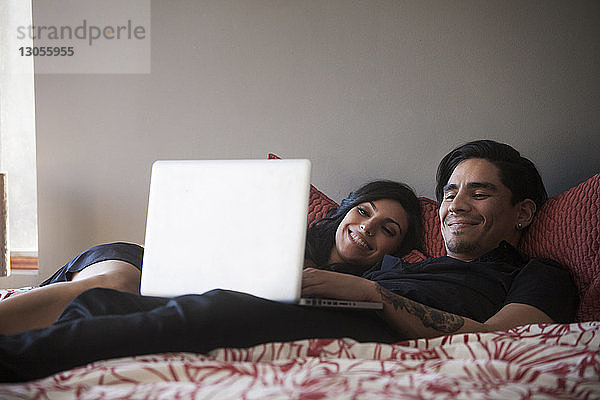 Lächelndes Paar benutzt Laptop-Computer  während es zu Hause im Bett liegt