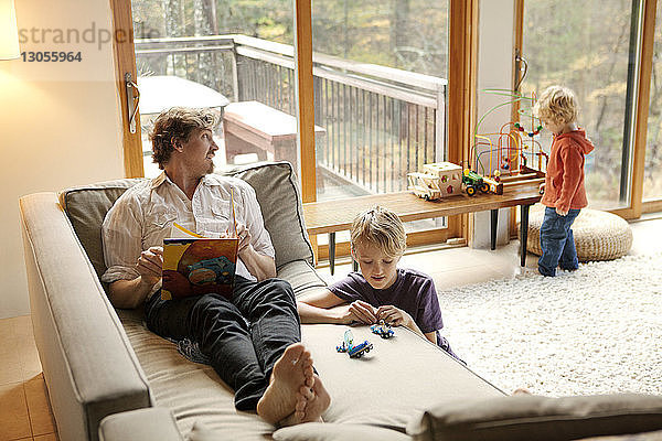 Vater hält Buch  während die Söhne zu Hause spielen