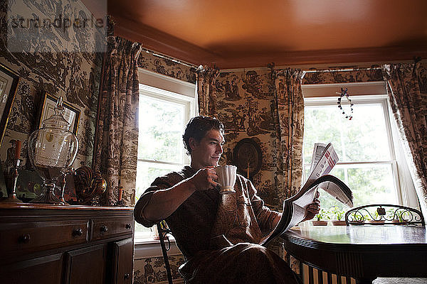 Mann liest Zeitung  während er zu Hause eine Teetasse hält