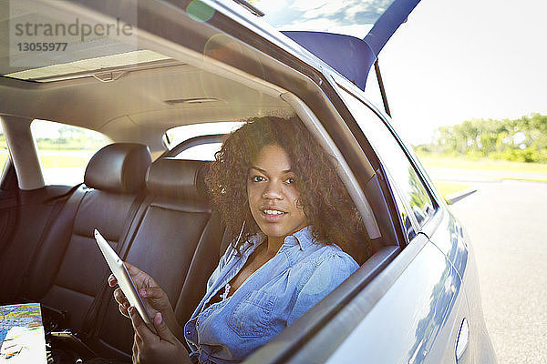 Porträt einer jungen Frau  die einen Tablet-Computer benutzt  während sie im Auto unterwegs ist