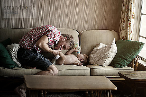 Vater küsst zu Hause auf dem Sofa die Füße eines kleinen Jungen