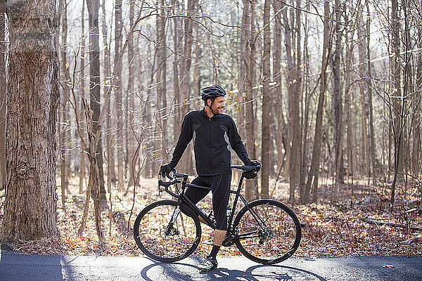 Radfahrer steht mit dem Fahrrad auf der Strasse im Wald