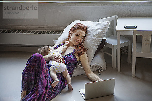 Mutter mit Mädchen benutzt Laptop  während sie zu Hause auf dem Boden liegt