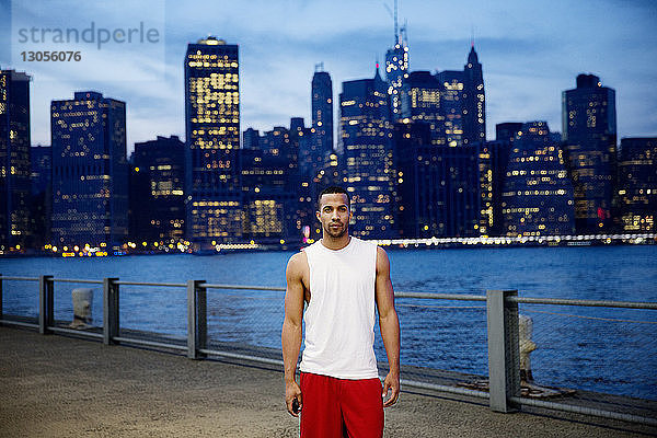 Porträt eines Sportlers  der in der Abenddämmerung auf der Promenade am East River in der Stadt steht