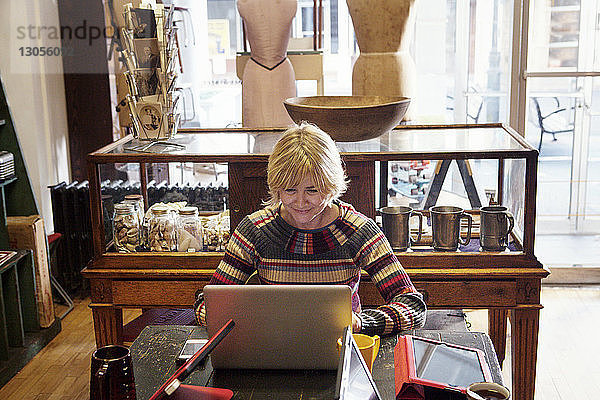 Glückliche Frau benutzt Laptop-Computer  während sie im Bekleidungsgeschäft sitzt