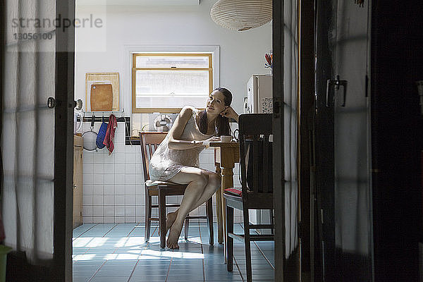 Schwangere Frau schaut weg  während sie auf einem Stuhl in der Küche sitzt