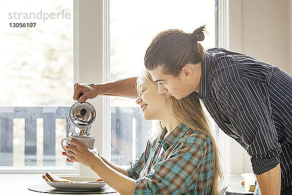 Mann gießt Kaffee in Tasse für Freundin zu Hause