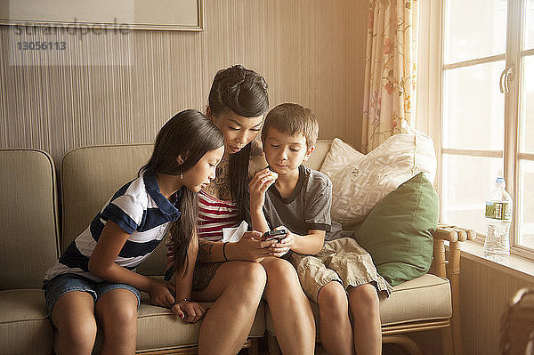 Mutter und Kinder telefonieren  während sie zu Hause auf dem Sofa sitzen