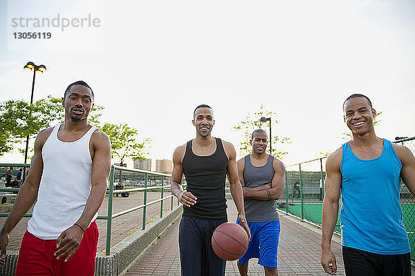 Porträt glücklicher Freunde mit Basketball beim Spaziergang auf einem Fußweg im Park