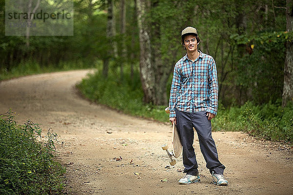 Porträt eines Mannes mit Skateboard auf einem Feldweg im Wald stehend