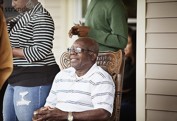 Glücklicher älterer Mann sitzt auf Stuhl von Frau  die auf der Veranda steht