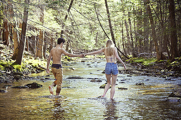 Junges Paar hält sich beim Gehen im Bach an den Händen