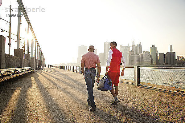 Rückansicht von Vater und Sohn beim Spaziergang auf der Promenade am East River in der Stadt