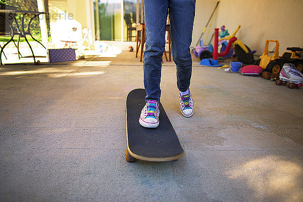 Untere Sektion von Mädchen  die im Hinterhof Skateboard fahren lernen