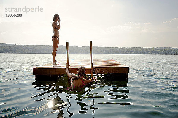 Freunde auf schwimmender Plattform im See gegen den Himmel an einem sonnigen Tag