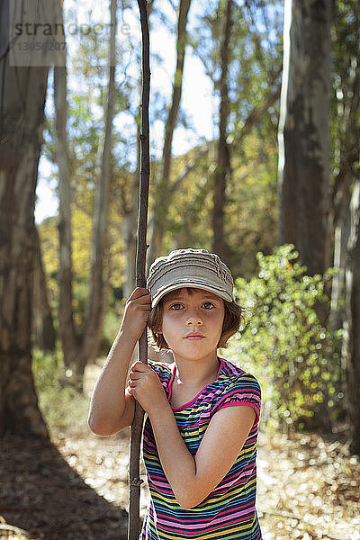 Porträt eines im Wald stehenden Mädchens  das einen Stock hält