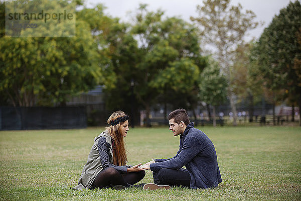 Paar hält Hände  während es auf einem Grasfeld im Park sitzt