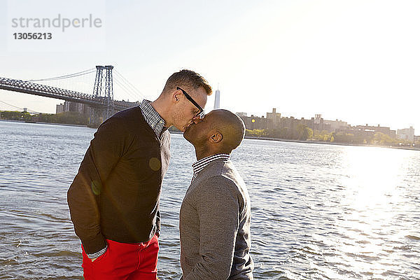 Schwule Männer küssen sich  während sie an einem sonnigen Tag am East River stehen