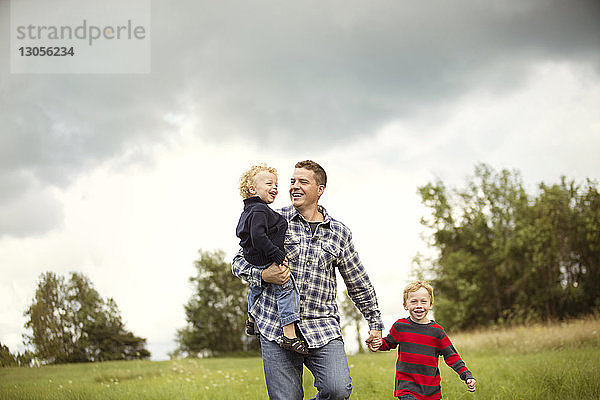 Lächelnder Vater mit Söhnen auf Grasfeld gegen den Himmel
