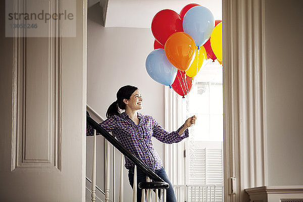 Glückliche Frau steht an der Treppe und hält Heliumballons