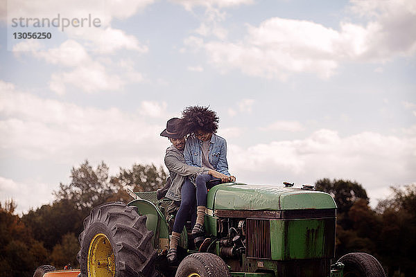 Frau sitzt mit einem Traktor fahrenden Mann vor bewölktem Himmel