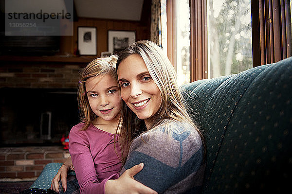 Porträt einer glücklichen Mutter  die ihre Tochter zu Hause auf dem Sofa umarmt