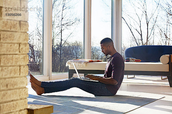 Mann benutzt Laptop  während er zu Hause auf dem Boden sitzt