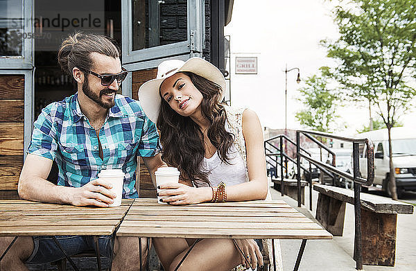 Glückliches Paar hält Einwegbecher und sitzt am Tisch im Straßencafé