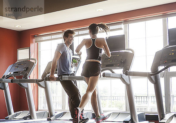 Glücklicher Mann schaut Frau an  die im Fitnessstudio auf dem Laufband läuft