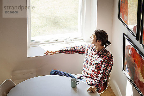 Draufsicht auf einen nachdenklichen Mann  der zu Hause am Fenster sitzt