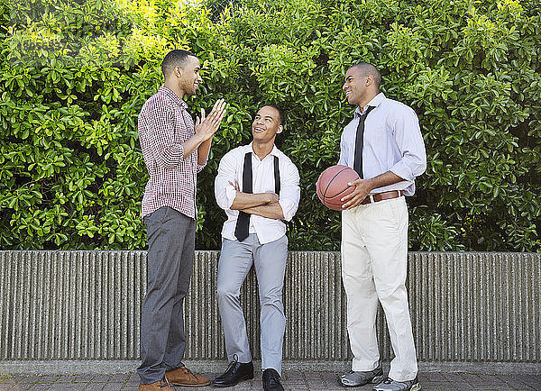 Lächelnder Mann hält Basketball in der Hand  während er mit Freunden gegen Pflanzen spricht