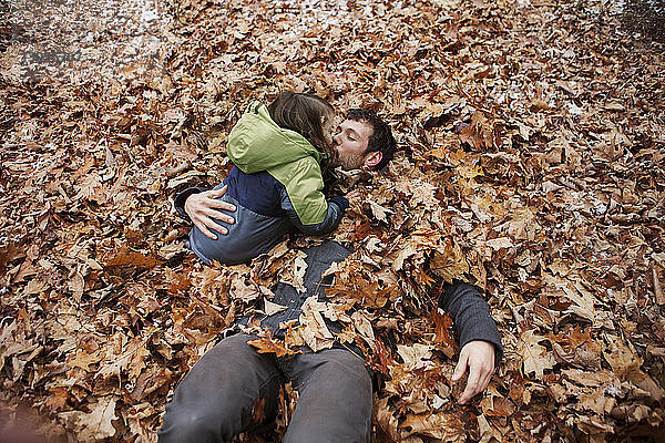Hochwinkelaufnahme eines Vaters  der seinen Sohn küsst  während er im Laub liegt