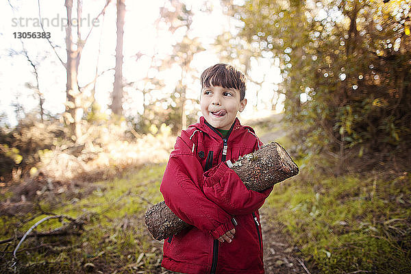 Junge schaut weg  während er einen Baumstamm im Wald hält