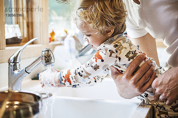 Ausgeschnittenes Bild eines Vaters  der seinen Sohn beim Händewaschen an der Küchenspüle hält