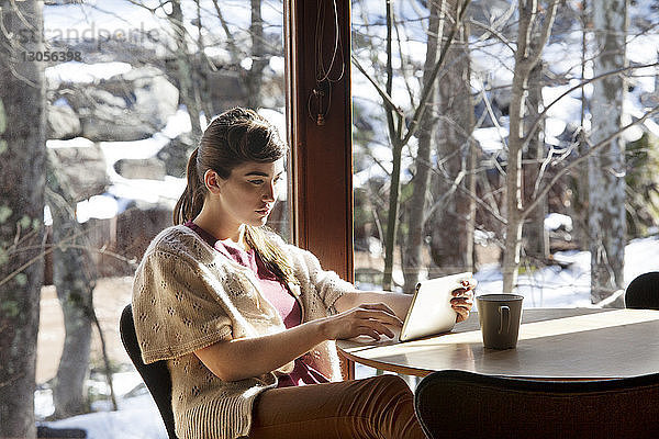 Frau benutzt Tablet-Computer  während sie auf einem Stuhl im Café sitzt