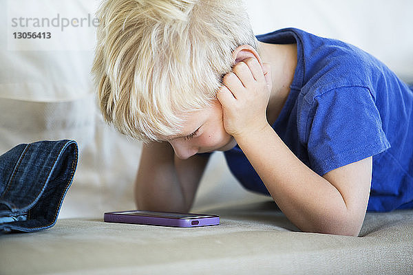 Junge schaut auf Smartphone im Bett