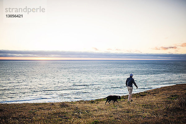 Mensch und Hund beim Spaziergang auf dem Feld am Meer gegen den Himmel