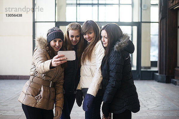 Freundinnen  die vor dem Gebäude stehen und sich per Smartphone selbstständig machen