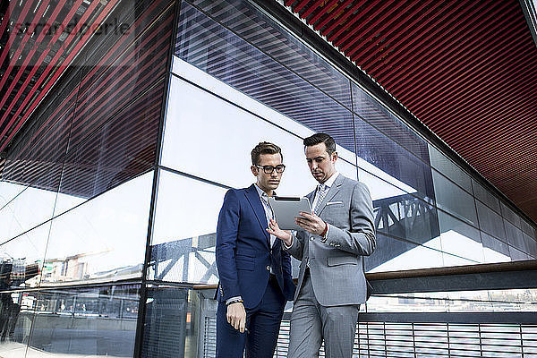Geschäftskollegen benutzen Tablet-Computer  während sie vor einem modernen Gebäude stehen